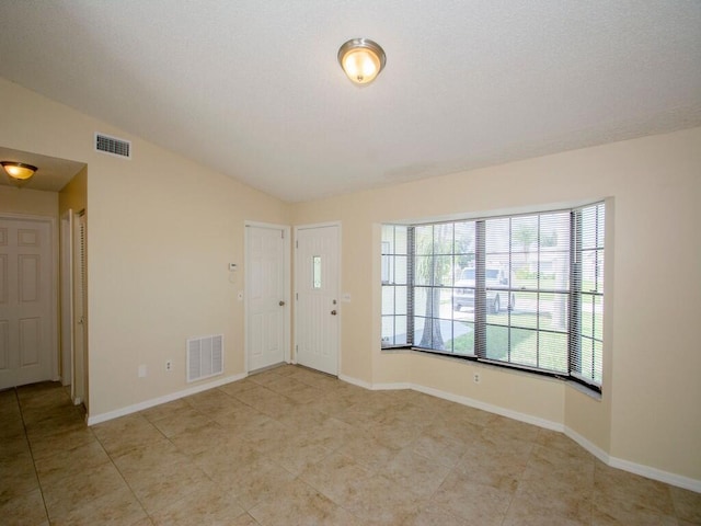 empty room featuring visible vents, baseboards, and vaulted ceiling