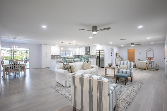 living room with recessed lighting, ceiling fan with notable chandelier, light wood-style floors, and baseboards