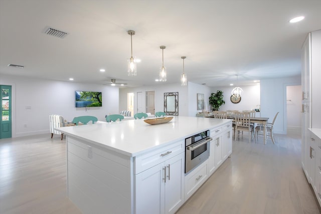 kitchen with light wood-style flooring, a kitchen island, visible vents, and oven