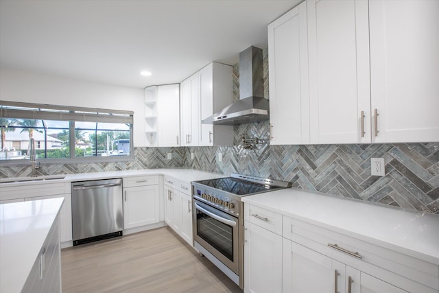 kitchen with backsplash, wall chimney range hood, stainless steel appliances, white cabinetry, and a sink