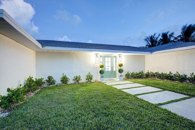 property entrance with french doors, a lawn, roof with shingles, and stucco siding