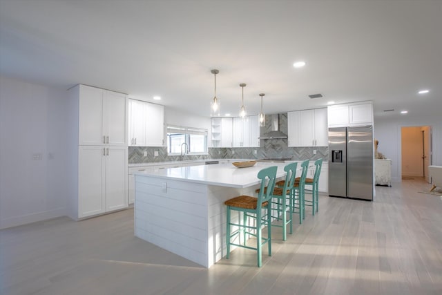 kitchen featuring backsplash, white cabinetry, stainless steel fridge, wall chimney exhaust hood, and light countertops