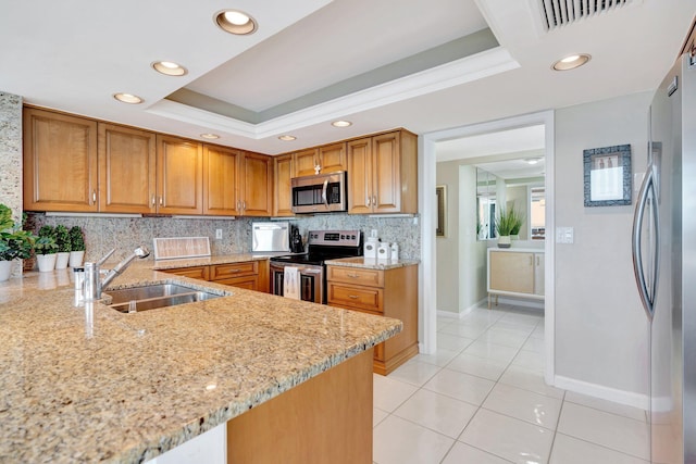 kitchen with a sink, backsplash, appliances with stainless steel finishes, a raised ceiling, and light stone countertops