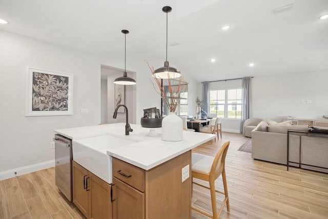 kitchen with a center island with sink, light wood finished floors, pendant lighting, stainless steel dishwasher, and open floor plan