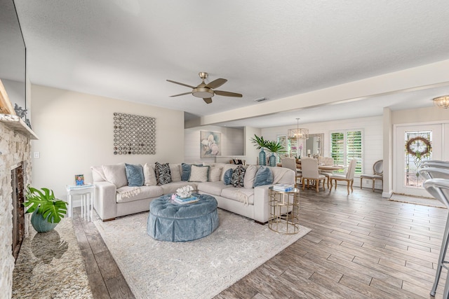 living area featuring a stone fireplace, wood finished floors, visible vents, and a textured ceiling