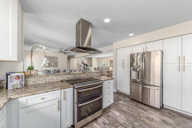 kitchen featuring appliances with stainless steel finishes, island exhaust hood, a peninsula, wood finished floors, and white cabinetry