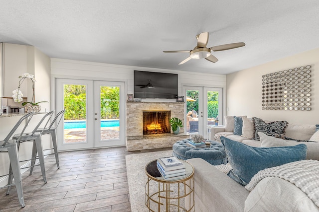 living area featuring wood tiled floor, a stone fireplace, french doors, a textured ceiling, and a ceiling fan