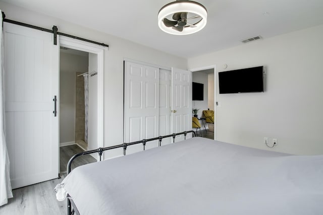 bedroom featuring visible vents, light wood finished floors, a closet, ensuite bathroom, and a barn door