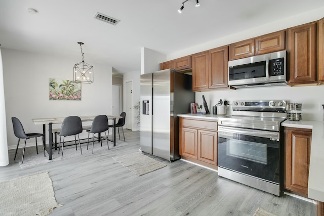 kitchen with brown cabinetry, visible vents, stainless steel appliances, light countertops, and light wood-type flooring