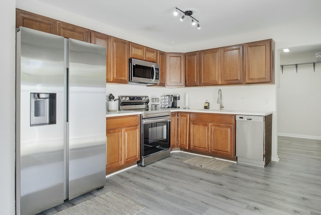 kitchen with brown cabinets, a sink, stainless steel appliances, light wood-style floors, and light countertops