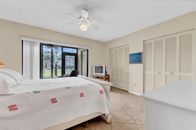 bedroom featuring light tile patterned floors, two closets, a ceiling fan, and a textured ceiling