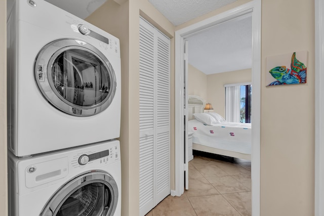 laundry area with laundry area, light tile patterned floors, stacked washer / drying machine, and a textured ceiling