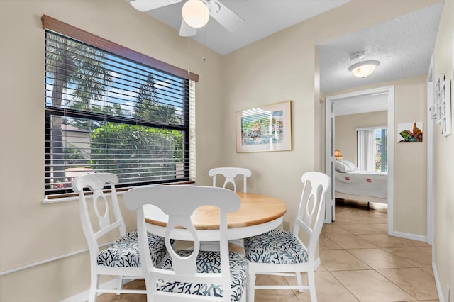 dining area with light tile patterned floors, baseboards, a textured ceiling, and ceiling fan