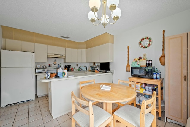 kitchen featuring black microwave, under cabinet range hood, a chandelier, a peninsula, and freestanding refrigerator