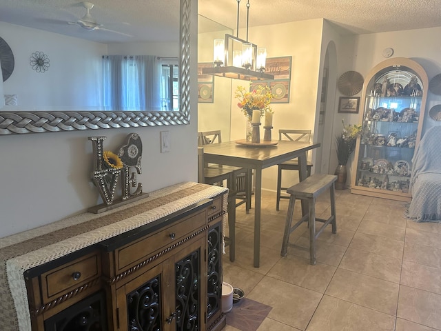 dining space with arched walkways, a ceiling fan, a textured ceiling, and light tile patterned flooring