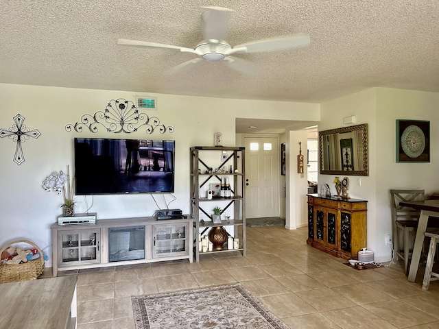 tiled living room featuring a textured ceiling, visible vents, and ceiling fan