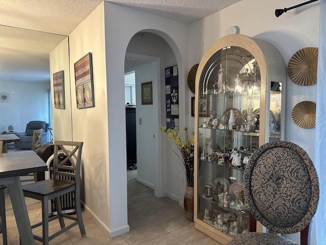 hallway with arched walkways, a textured ceiling, and tile patterned flooring