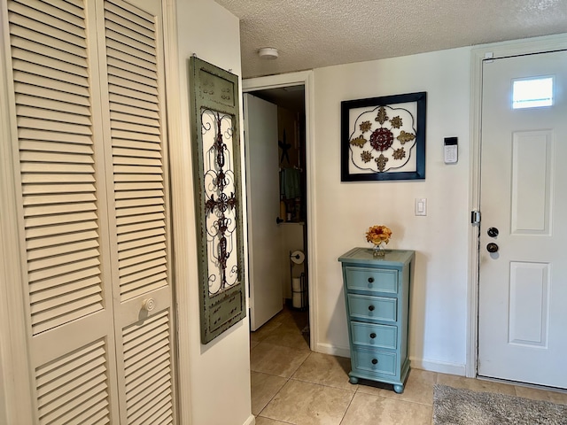 doorway with a textured ceiling, baseboards, and light tile patterned floors