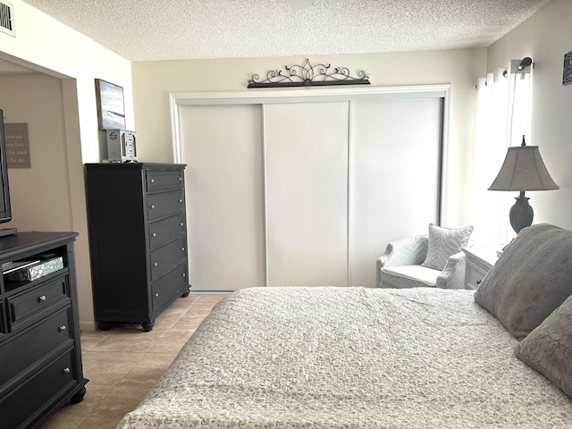 bedroom with light tile patterned flooring, visible vents, a closet, and a textured ceiling