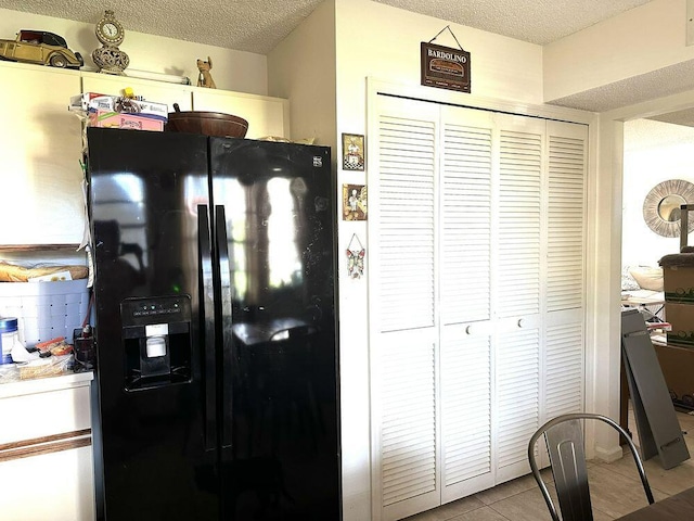 kitchen with light tile patterned floors, a textured ceiling, and black refrigerator with ice dispenser