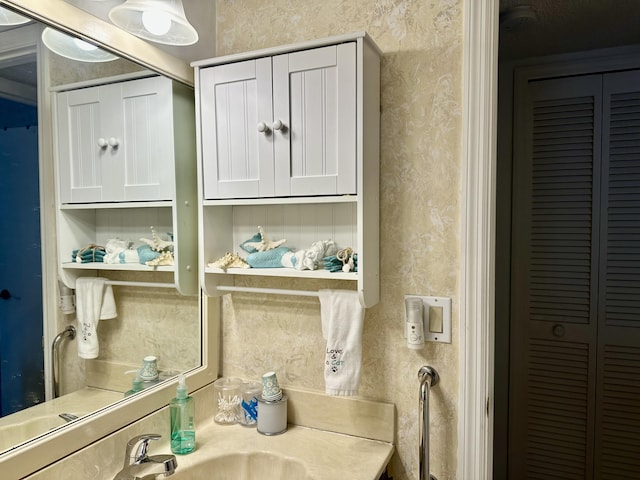 bathroom with a closet, wallpapered walls, and a sink