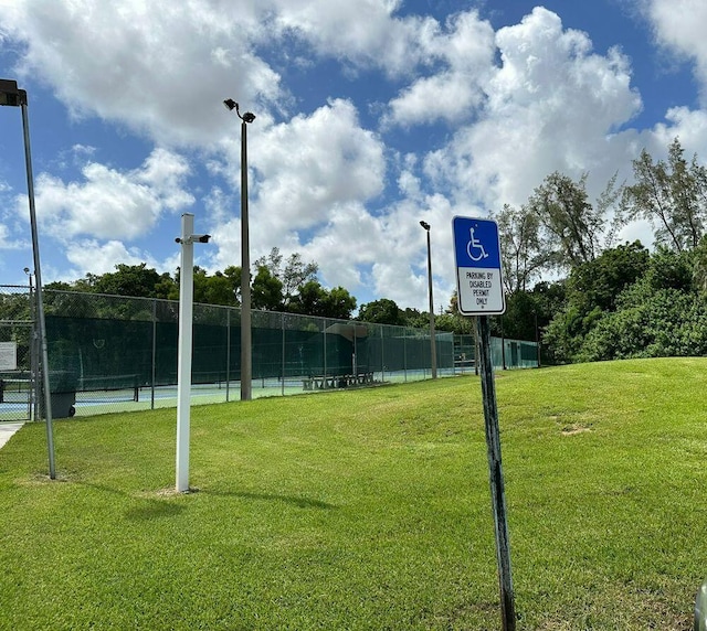view of home's community featuring a lawn, a tennis court, and fence