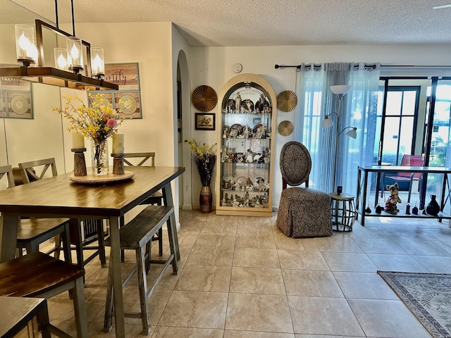 dining room with tile patterned floors, arched walkways, and a textured ceiling