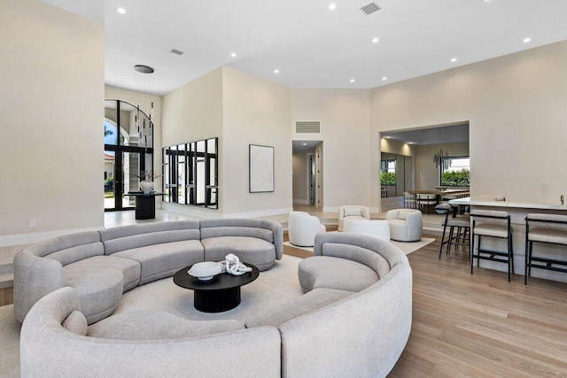 living room with light wood finished floors, visible vents, recessed lighting, and a towering ceiling