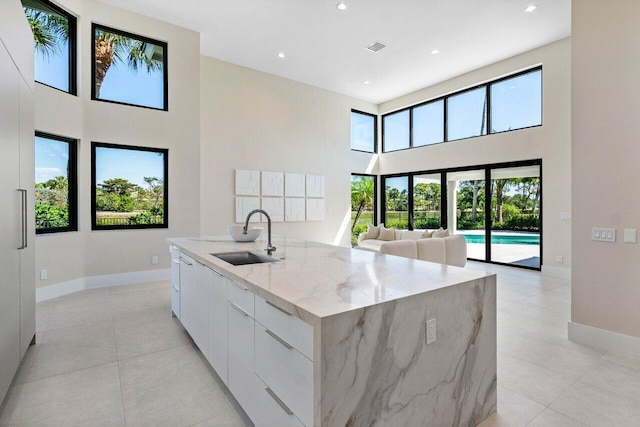 kitchen featuring light stone countertops, a large island, white cabinets, modern cabinets, and a sink