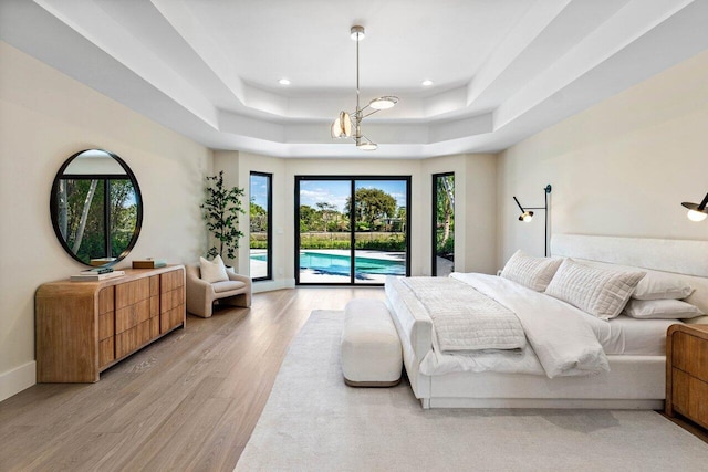 bedroom featuring access to outside, a tray ceiling, recessed lighting, light wood-style floors, and baseboards