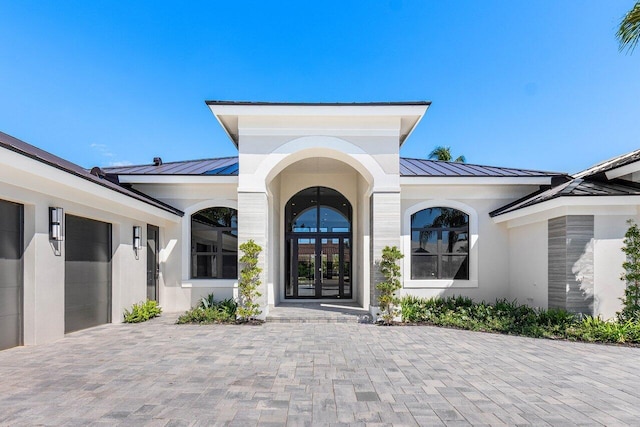 property entrance with a standing seam roof, an attached garage, decorative driveway, and metal roof