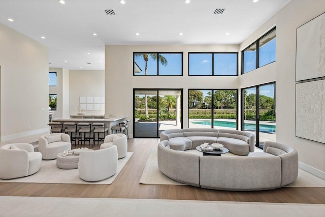 living area with recessed lighting, visible vents, a high ceiling, and wood finished floors