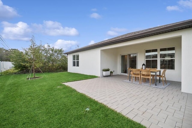 rear view of house with stucco siding, a patio, a yard, and fence