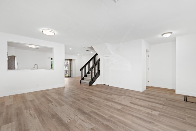 unfurnished living room featuring light wood-type flooring, stairs, and baseboards