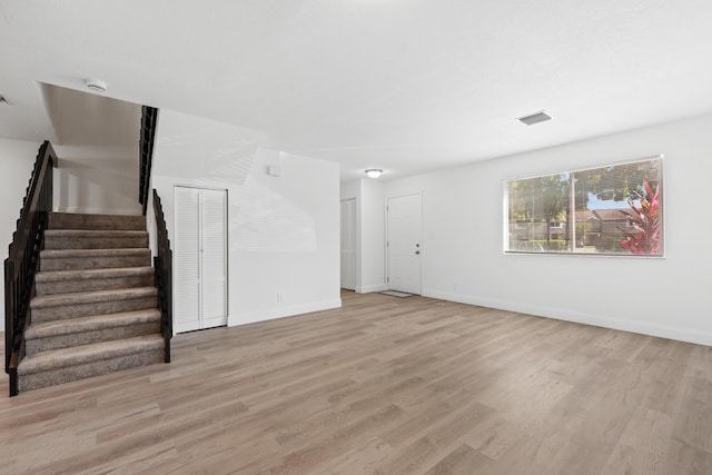 unfurnished living room with visible vents, light wood-style flooring, stairway, and baseboards