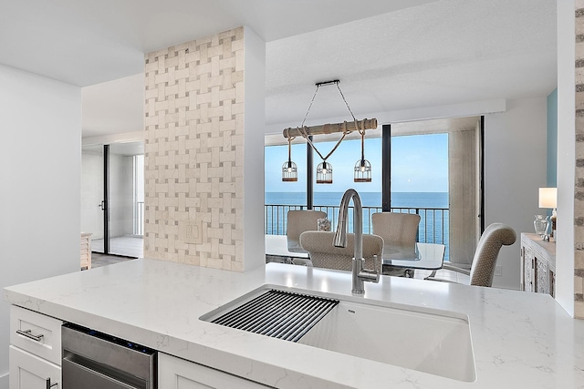 kitchen with backsplash, a water view, light stone counters, white cabinets, and a sink