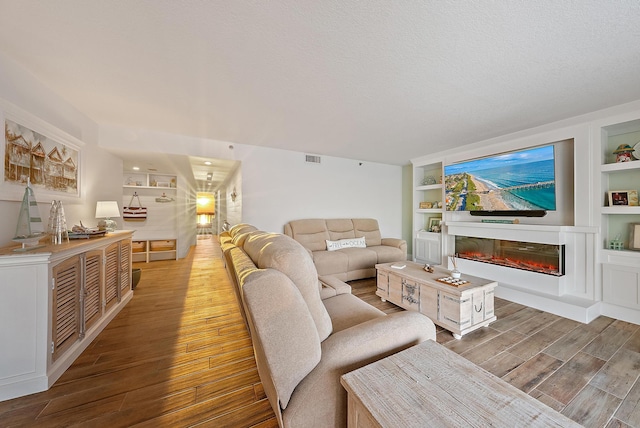 living room with a glass covered fireplace, a textured ceiling, built in features, and wood finished floors