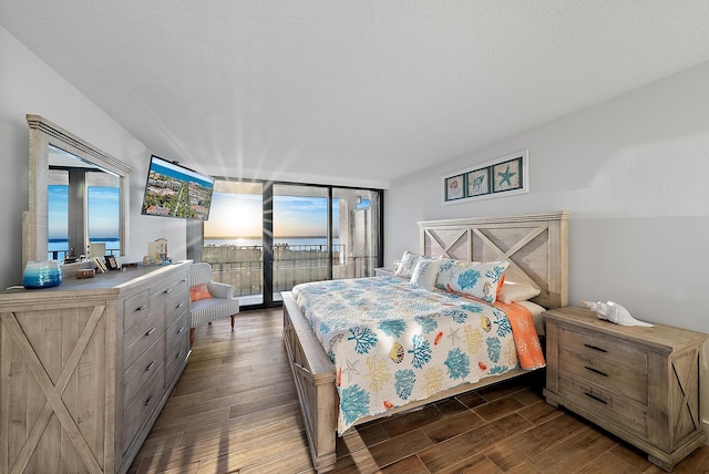 bedroom with a wall of windows, access to outside, wood finished floors, and a textured ceiling