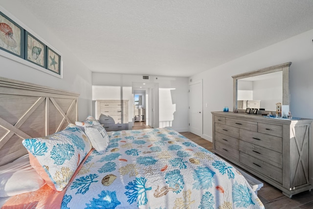 bedroom featuring visible vents, a textured ceiling, baseboards, and wood finished floors