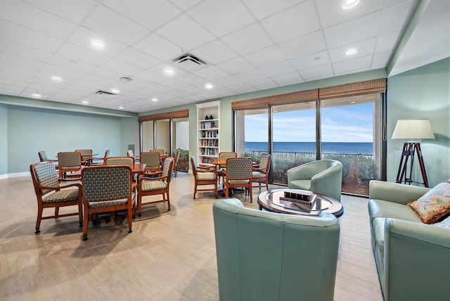 living room featuring visible vents, a water view, a drop ceiling, and baseboards