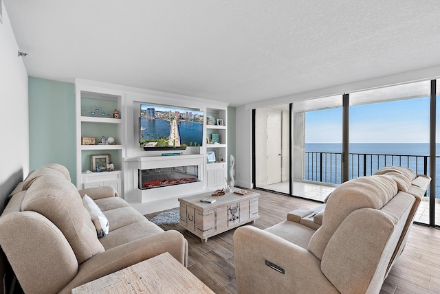 living area featuring built in shelves, a wall of windows, wood finished floors, a glass covered fireplace, and a textured ceiling
