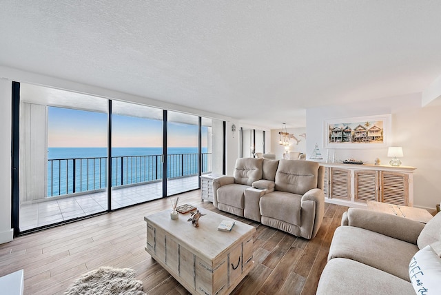 living room with a wall of windows, a water view, a textured ceiling, and wood finished floors