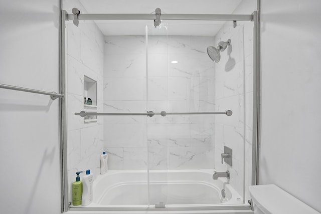 bathroom featuring toilet and bath / shower combo with glass door