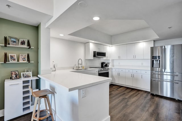 kitchen featuring dark wood-type flooring, a sink, stainless steel appliances, a peninsula, and white cabinets