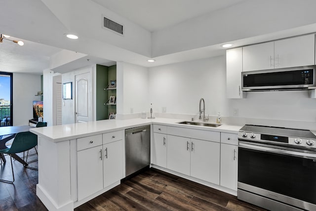 kitchen featuring visible vents, a peninsula, a sink, dark wood-type flooring, and appliances with stainless steel finishes