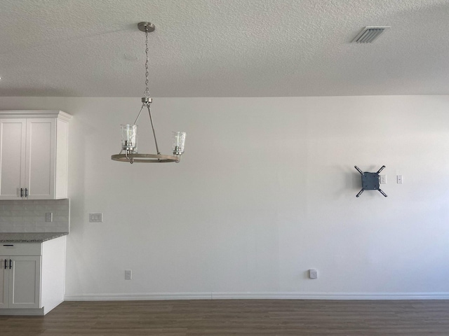 unfurnished dining area with visible vents, baseboards, dark wood finished floors, an inviting chandelier, and a textured ceiling