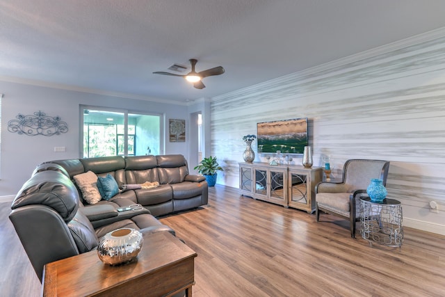 living room with wood finished floors, a ceiling fan, visible vents, baseboards, and crown molding