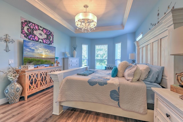 bedroom with a raised ceiling, a notable chandelier, wood finished floors, and crown molding