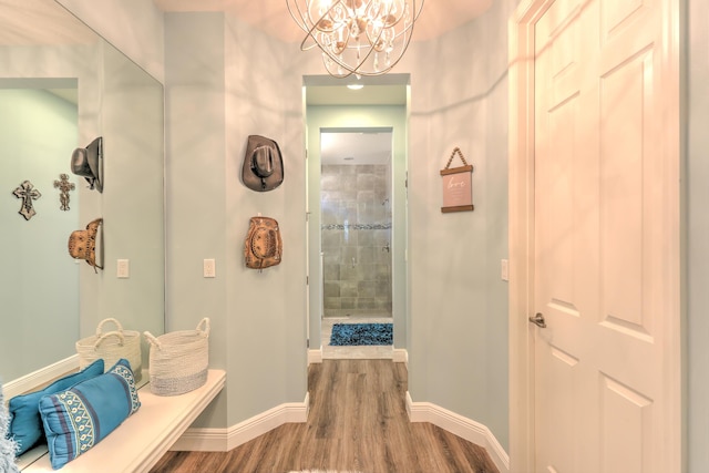 bathroom featuring wood finished floors, baseboards, a tile shower, and a chandelier