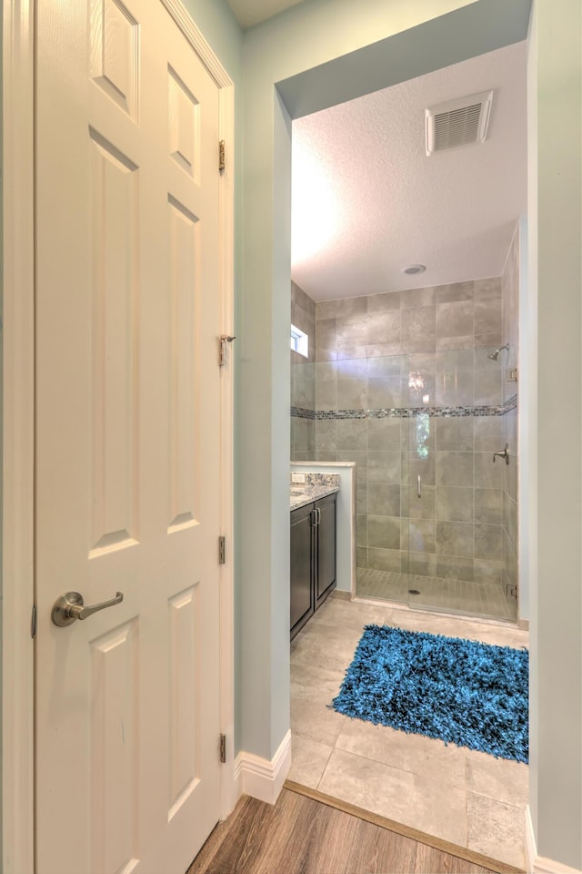 full bath with vanity, wood finished floors, baseboards, visible vents, and a stall shower